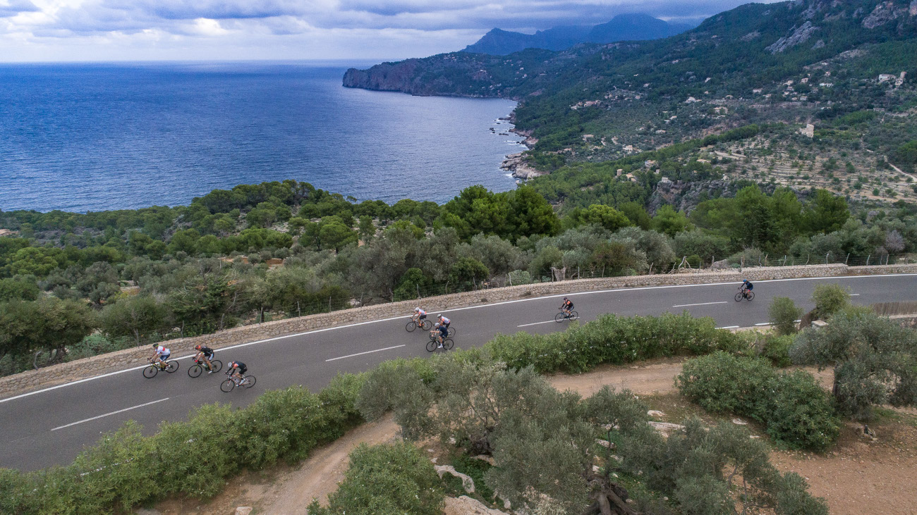 Cyclists riding along a road in Majorca, with the coastline and the sea in the background