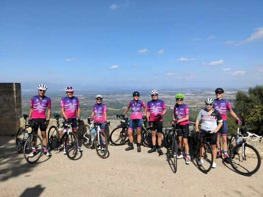 8 cyclists posing at the top of a climb, with a view of Majorca in the background